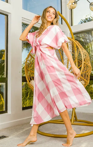Model twirling in a pink checkered front tied puff sleeve dress with cut outs, showcasing a playful and modern style.