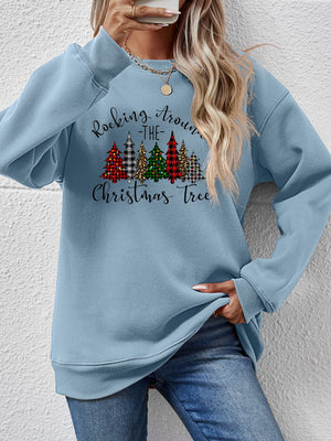 Woman wearing a blue Christmas tree graphic sweatshirt with 'Rocking Around the Christmas Tree' design.