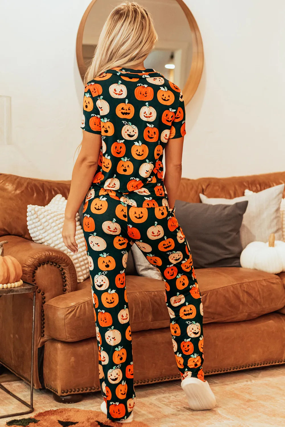 Back view of a woman wearing a pumpkin printed short sleeve top and pants lounge set, sitting on a cozy couch.