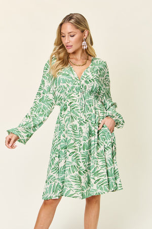 Model wearing green palm leaf printed dress with pockets, ruched detailing, and balloon sleeves against a light background.