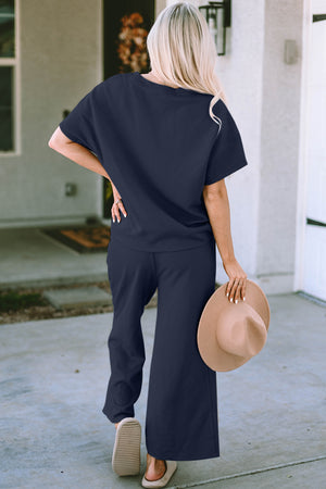Model in navy double take two-piece texture set with short sleeves and wide-leg pants, stylishly holding a hat.