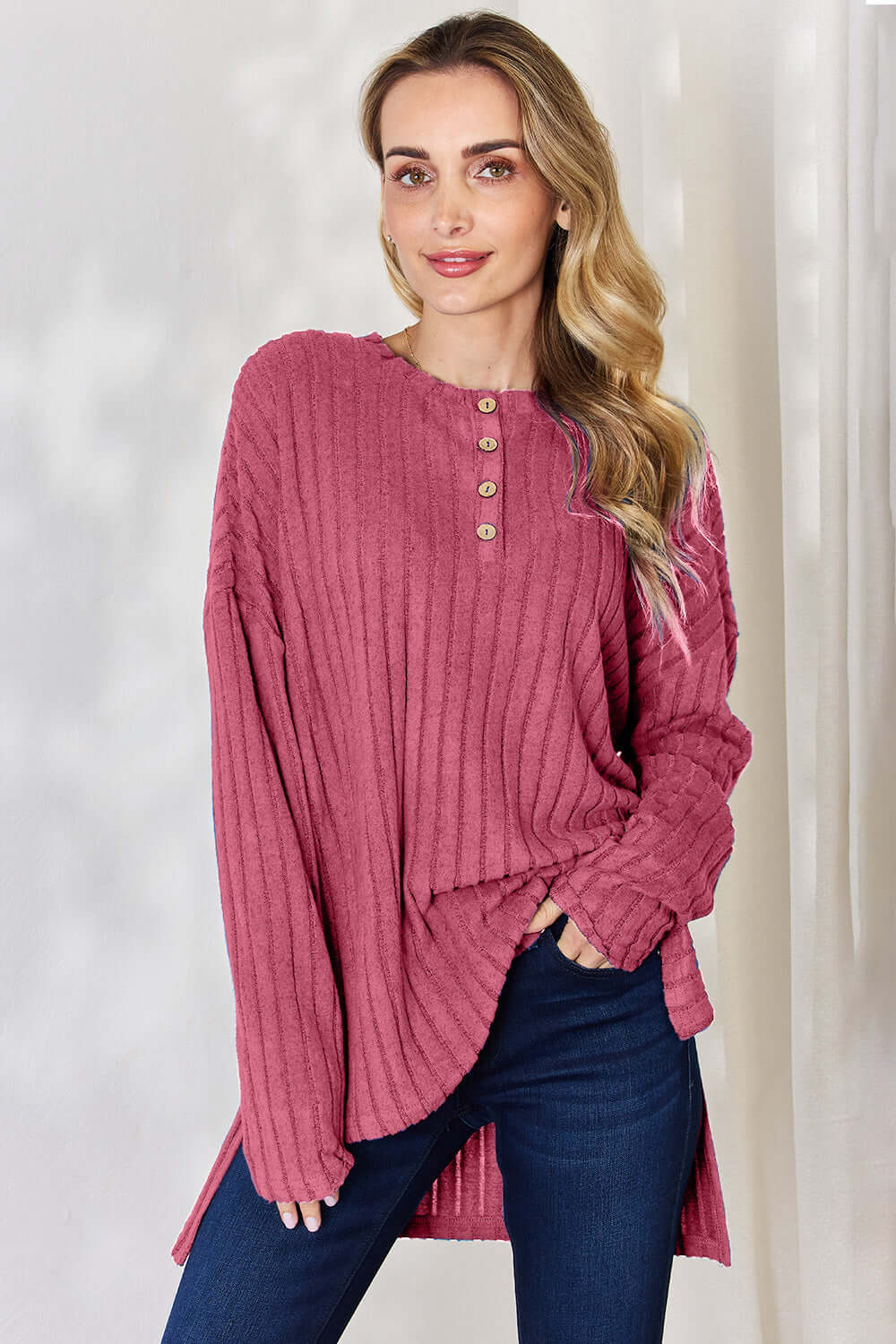 Model wearing a pink ribbed long sleeve high-low t-shirt with buttons, paired with dark jeans.