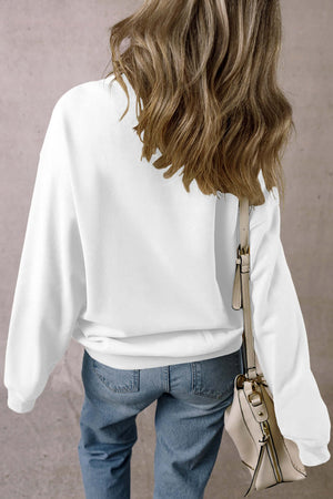 Back view of a woman wearing a white long sleeve sweatshirt paired with blue jeans and carrying a bag.