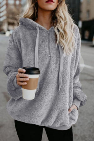 Woman wearing a cozy gray quarter-zip teddy hoodie, holding a coffee cup in a city setting.