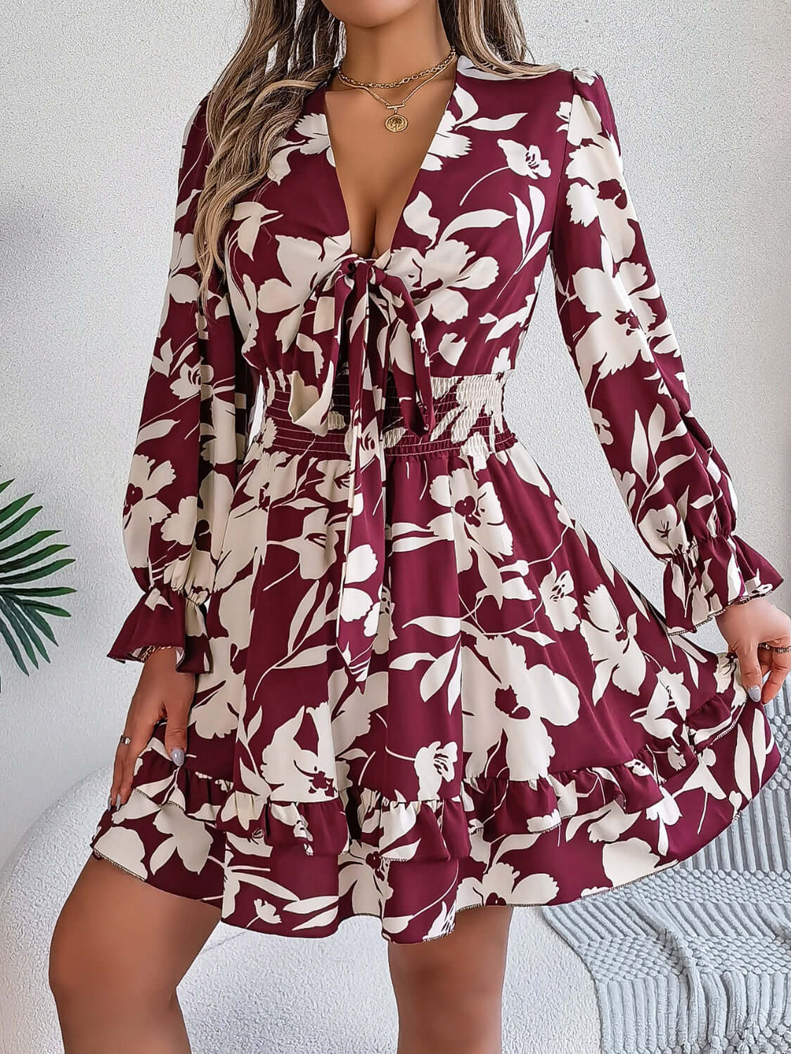 Tied ruffled long sleeve dress in burgundy with floral print, featuring a fitted waist and flared skirt.