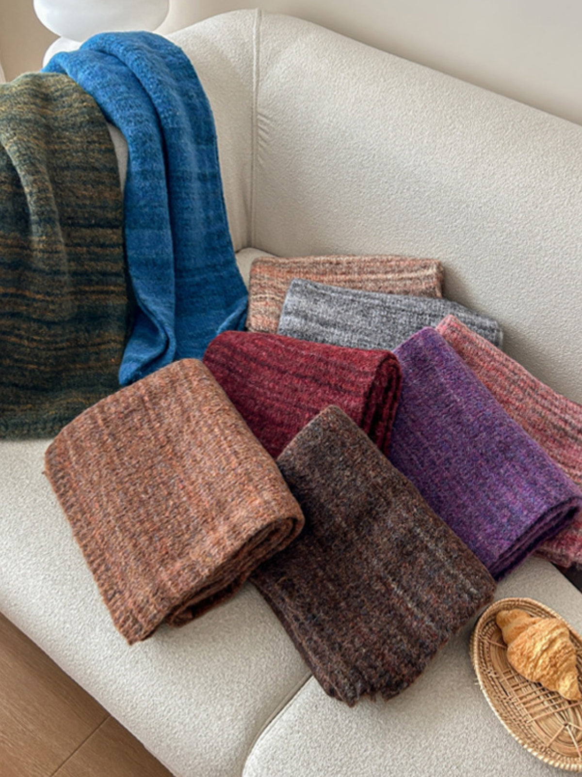 Colorful assortment of striped detail knit scarves in cozy materials displayed on a sofa, perfect for winter fashion.