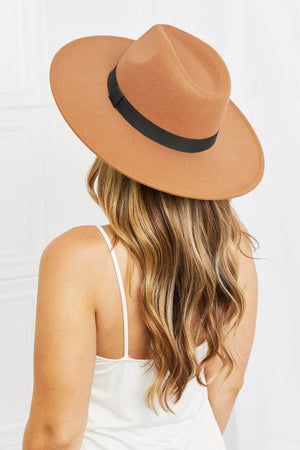 Woman wearing a tan fedora hat with a black ribbon band, showcasing its stylish design from the back.