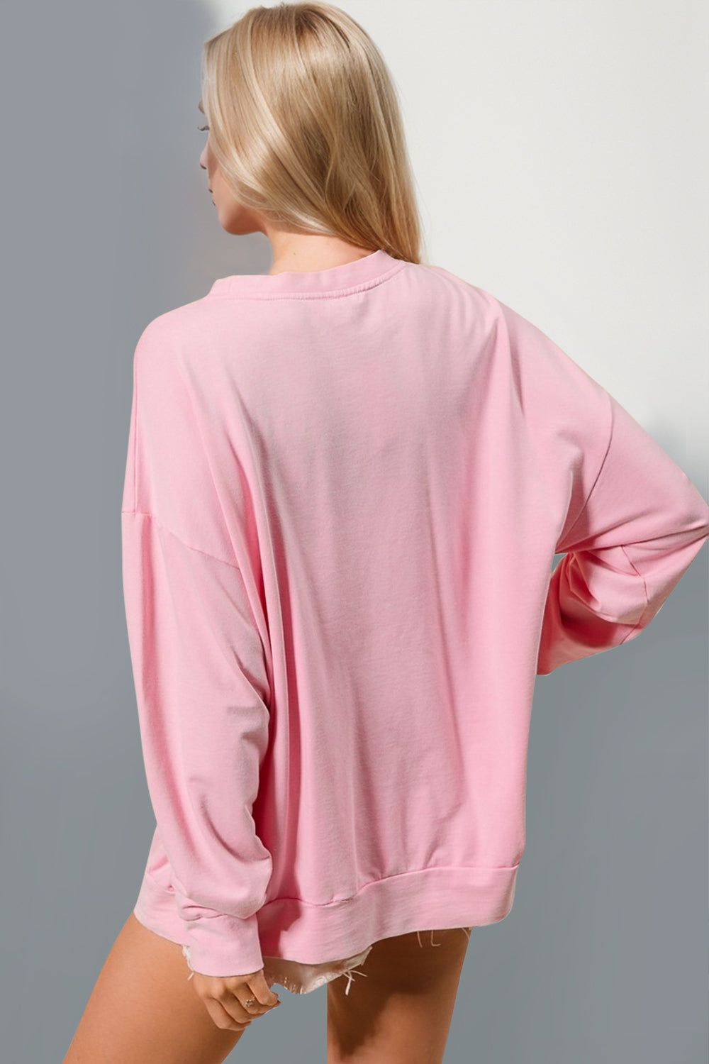 Back view of a model wearing a pink long sleeve sweatshirt with a relaxed fit and round neckline.