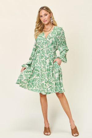 Model wearing a green printed ruched balloon sleeve dress, showcasing tropical leaf patterns and a relaxed fit.