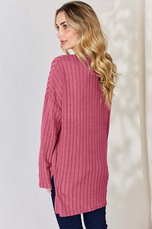 Back view of woman in a ribbed pink long sleeve high-low t-shirt, showcasing its stylish slit design.