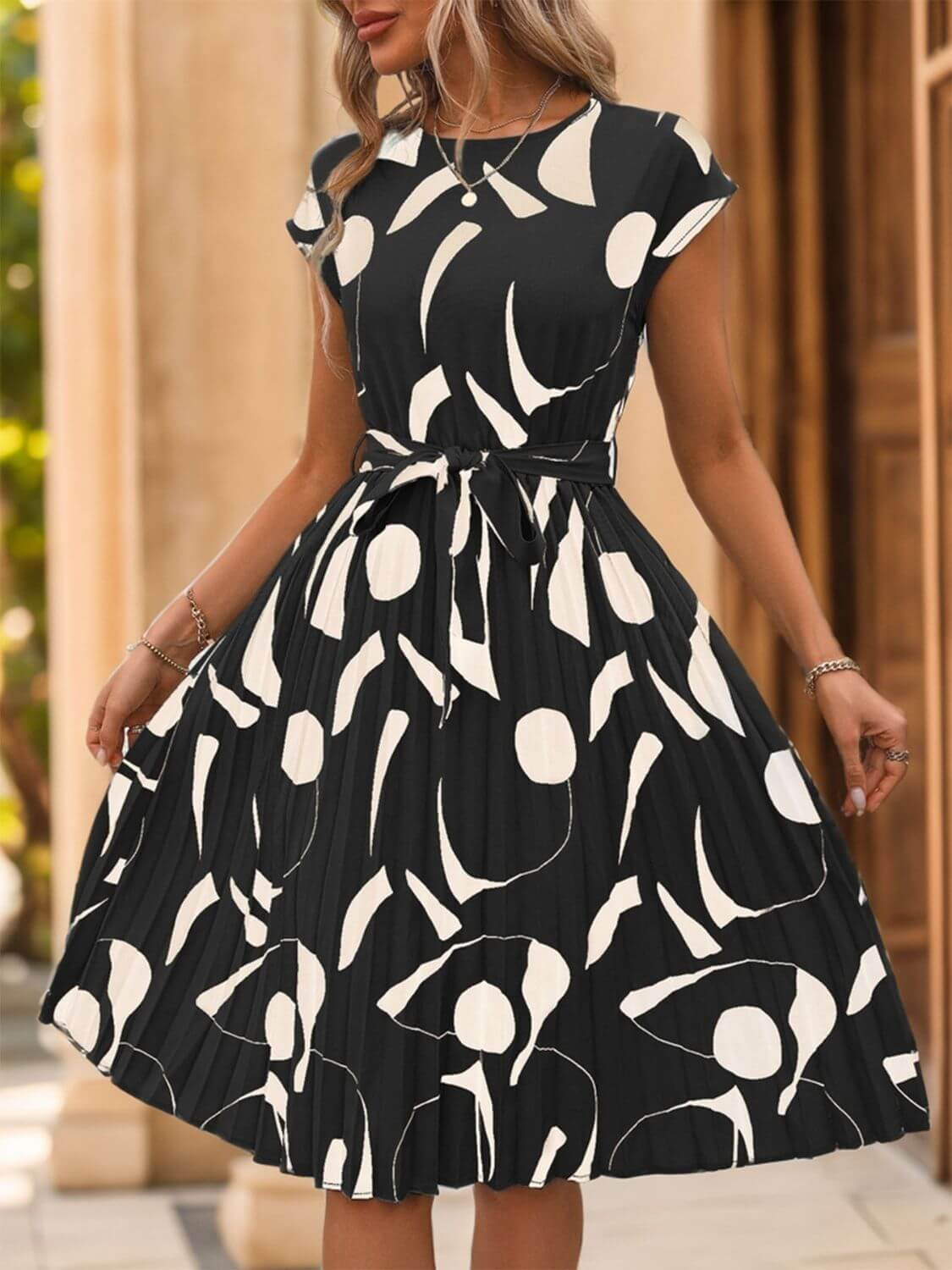 Tied pleated cap sleeve dress in black with white abstract print, perfect for casual or semi-formal occasions.
