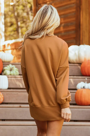 Back view of a woman in a cozy brown long sleeve sweatshirt, surrounded by pumpkins in an autumn setting.