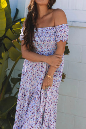 Woman wearing a tiered floral shirred high waist maxi dress with off-the-shoulder sleeves and light blue floral print.