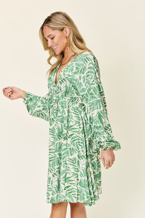 Model wearing a green printed ruched balloon sleeve dress, showcasing a stylish design with a tropical leaf pattern.