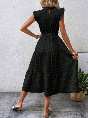Back view of a model wearing a tied ruffled cap sleeve midi dress in black, showcasing its flowy silhouette and tiers.