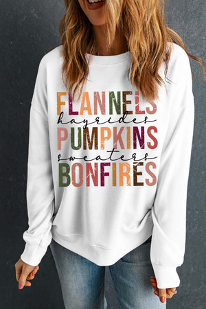 Woman wearing a white sweatshirt featuring colorful text: "Flannels, Hayrides, Pumpkins, Sweaters, Bonfires".