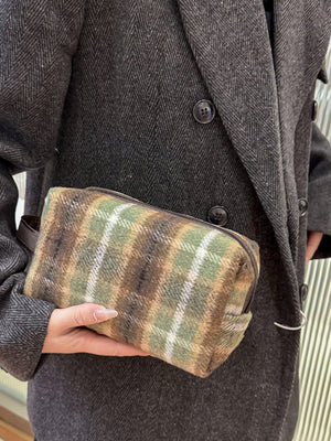 Contrast plaid clutch bag with zipper in a green and brown color scheme, held by a person in a stylish coat.