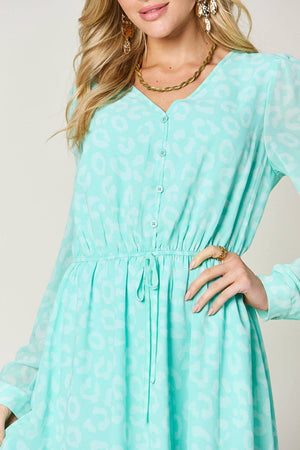 Close-up of a woman wearing a mint green ruched V-neck dress with button details and sheer long sleeves.
