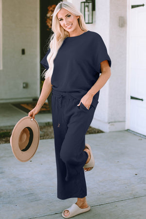 Woman wearing Double Take two-piece navy top and pants set, showcasing casual style with a hat and relaxed fit.