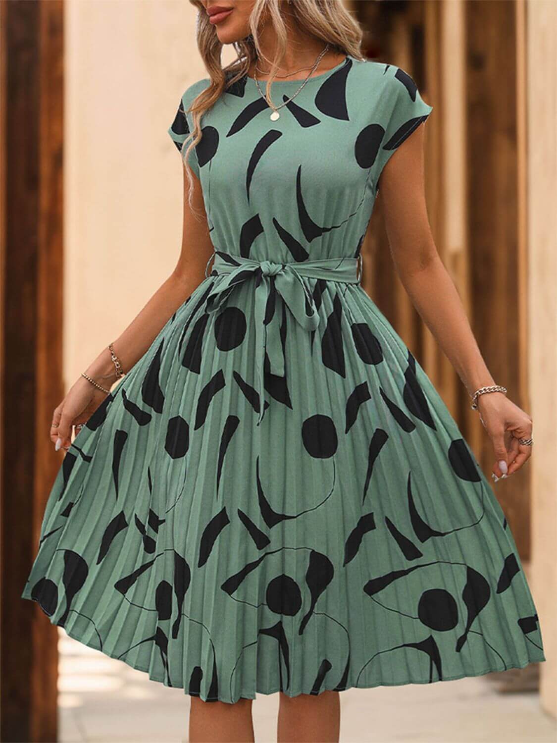 Tied pleated cap sleeve dress in green with black print, featuring a feminine silhouette and stylish design.
