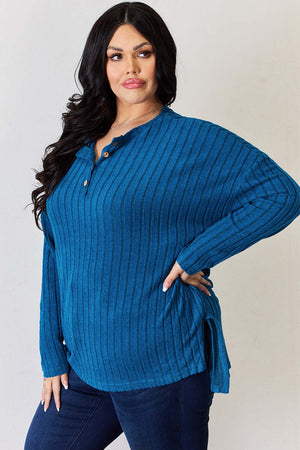 Curvy model wearing a blue ribbed high-low T-shirt with half buttons and side slits.