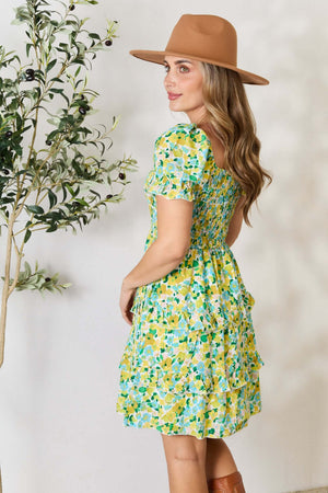 Model wearing a floral smocked scoop neck mini dress with flounce sleeves and a stylish hat, showcasing a vibrant and playful design.