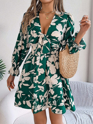 Tied ruffled printed long sleeve dress in green floral design, paired with a woven bag, perfect for casual outings.