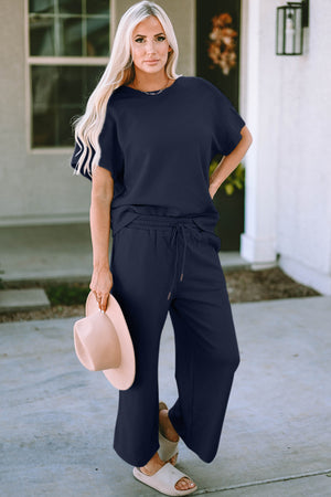 Model wearing a navy two-piece outfit featuring a short sleeve top and drawstring pants, perfect for casual styling.