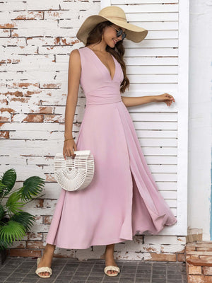 Stylish woman wearing a full size slit v-neck sleeveless midi dress in soft pink, paired with a wide-brim hat and chic accessories.