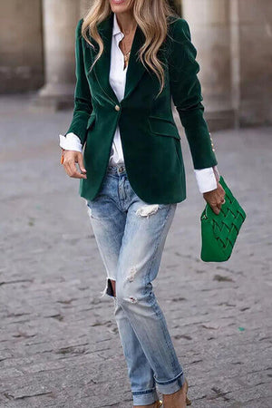 Chic woman wearing a green lapel collar blazer, white shirt, and distressed jeans, holding a green clutch.