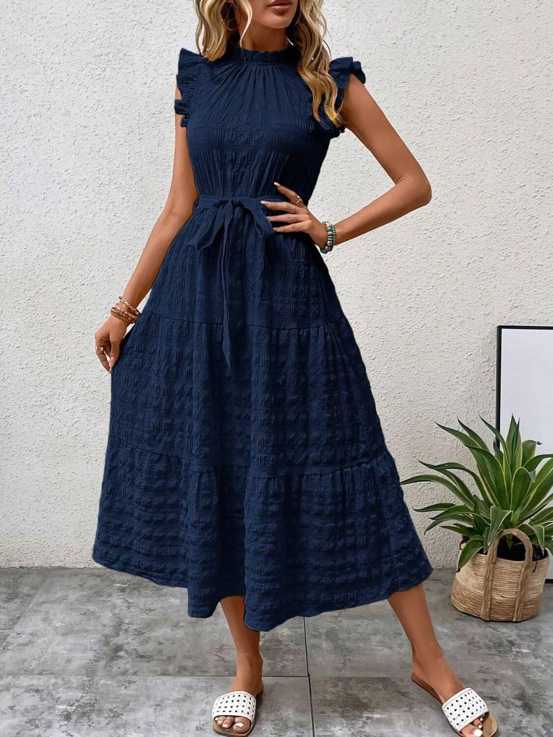 Tied ruffled cap sleeve navy midi dress styled with accessories and a plant background.