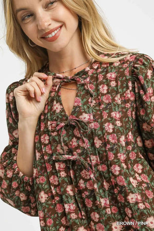 Close-up of a woman smiling in a floral tie-neck babydoll dress featuring a brown and pink pattern.