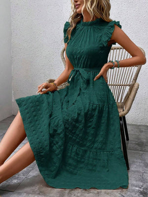 Model wearing a tied ruffled cap sleeve midi dress in green, styled with a trendy chair.