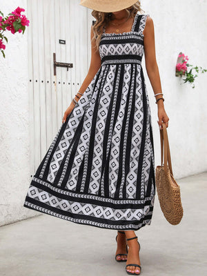 Fashionable printed wide strap cami dress, ankle-length, styled with a straw bag and summer hat, perfect for warm occasions.