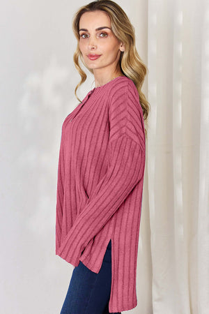 Model wearing a pink ribbed high-low long sleeve t-shirt with button detail and side slits.