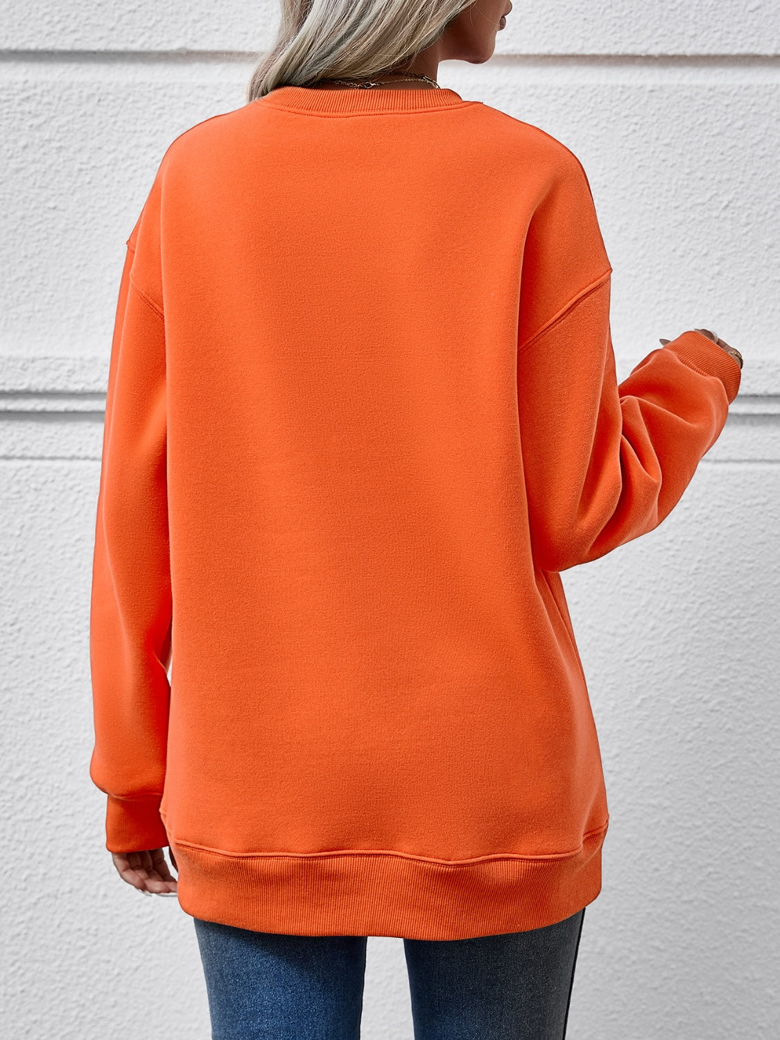 Back view of a woman wearing an orange round neck sweatshirt, showcasing its relaxed fit and cozy style.