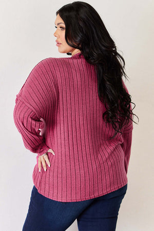Plus size model wears a ribbed, long sleeve, high-low t-shirt in pink, showcasing the back design and relaxed fit.