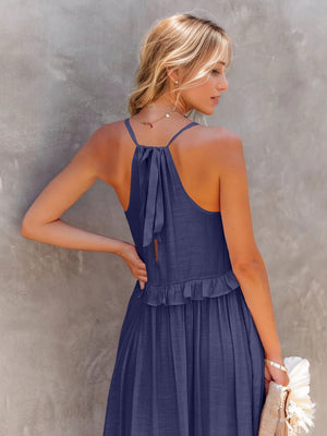 Back view of woman wearing a navy ruffled sleeveless tiered maxi dress with a tied neckline and subtle detailing.