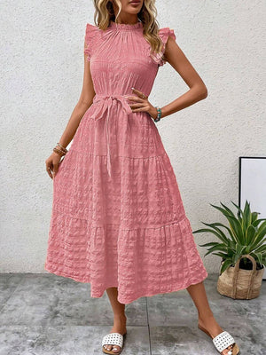 Feminine tied ruffled cap sleeve midi dress in soft pink, styled with chic sandals and a natural background.