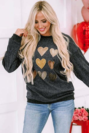 Woman wearing a black heart print round neck sweatshirt, styled with blue jeans and smiling.