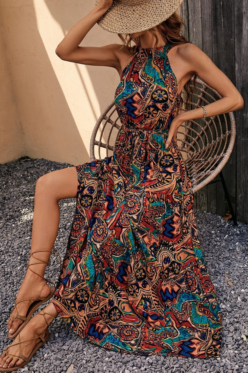 Model wearing a vibrant Tied Slit Floral Sleeveless Dress, styled with sandals and a sun hat, perfect for summer outings.