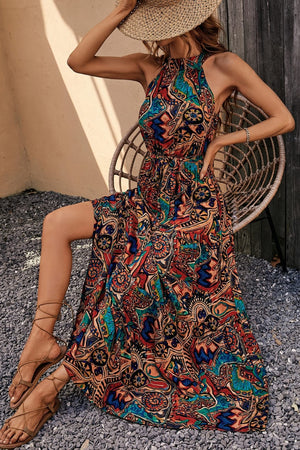 Model wearing a vibrant Tied Slit Floral Sleeveless Dress, styled with sandals and a sun hat, perfect for summer outings.