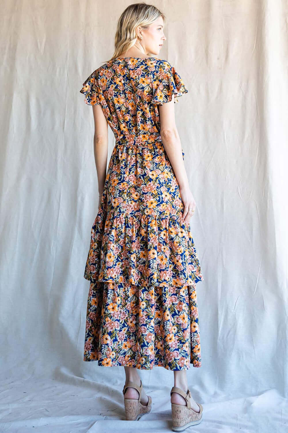 Back view of a woman wearing a floral ruffled midi dress by Nu Label, showcasing vibrant patterns and elegant ruffles.
