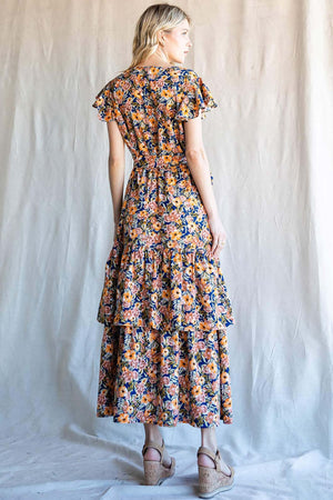 Back view of a woman wearing a floral ruffled midi dress by Nu Label, showcasing vibrant patterns and elegant ruffles.