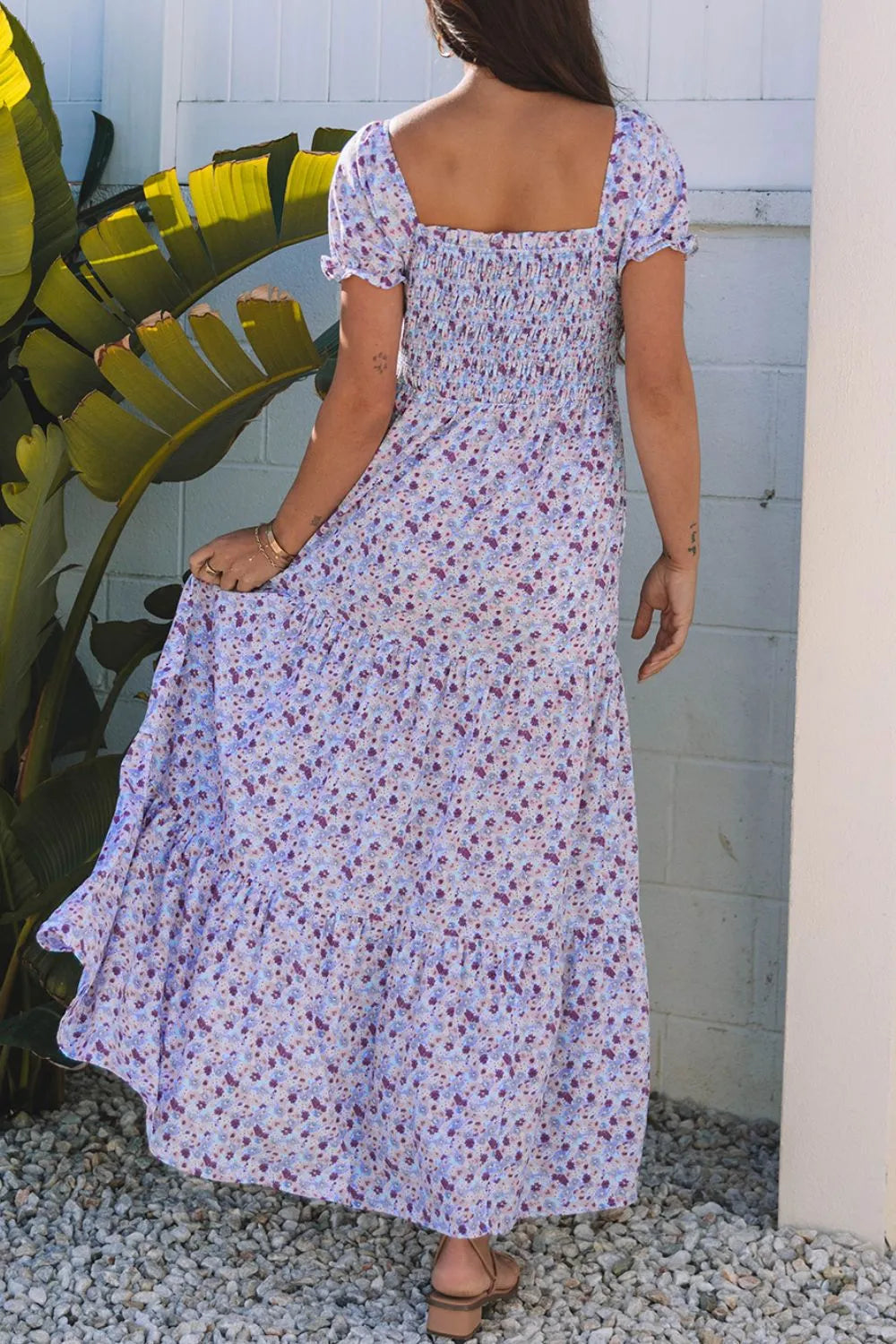 Model in a tiered floral shirred high waist maxi dress, showcasing the back design amid tropical plants.