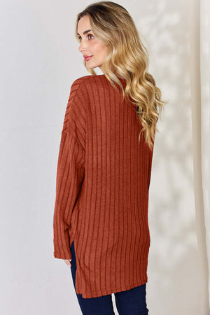 Back view of a woman in a rust-colored ribbed high-low long sleeve t-shirt, styled with dark jeans.