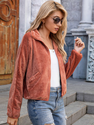 Model wearing a zip-up collared jacket with pockets, styled with sunglasses and casual denim shorts.