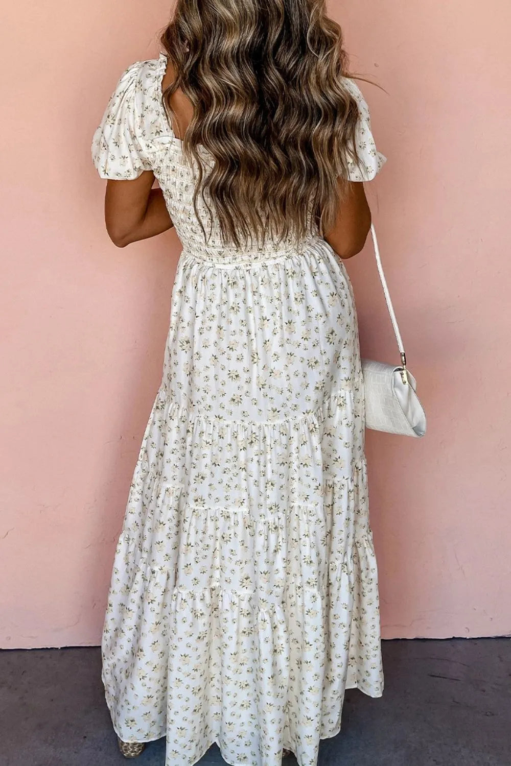 Back view of a women’s floral smocked short puff sleeve maxi dress against a pink wall.