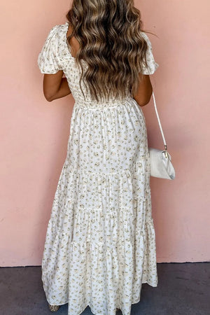 Back view of a women’s floral smocked short puff sleeve maxi dress against a pink wall.