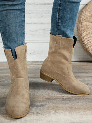 Pair of Western style block heel boots in beige suede, worn with blue jeans, showcasing low heels and comfortable fit.